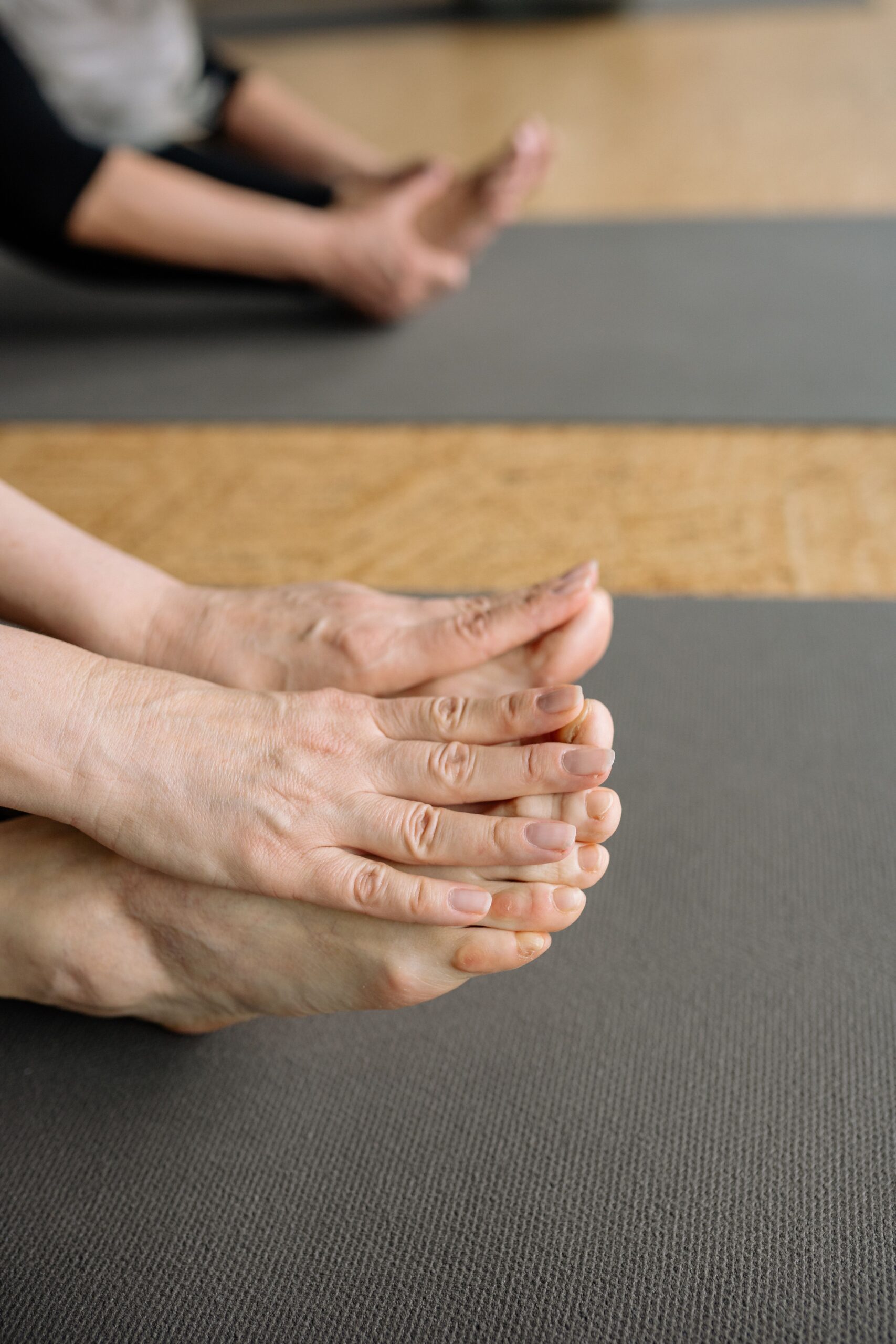 Close-up of hands touching feet in a yoga stretch on a mat, focus on flexibility.